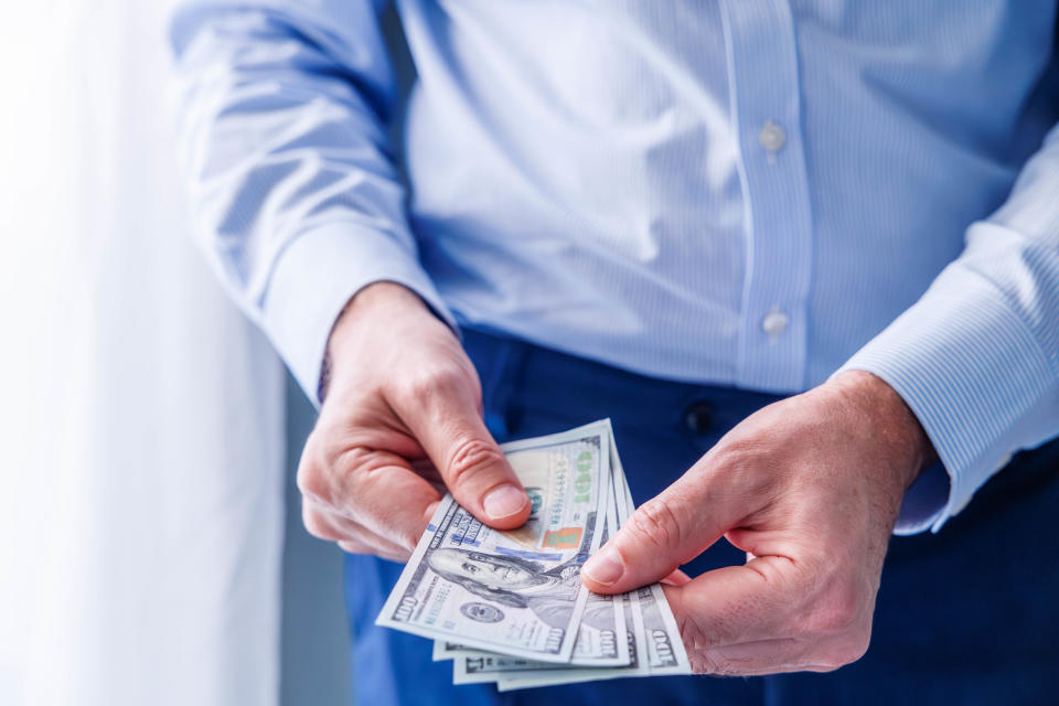 Close-up of man's hands in a light blue shirt holding U.S. dollar banknotes in front of him. Business and finance concept