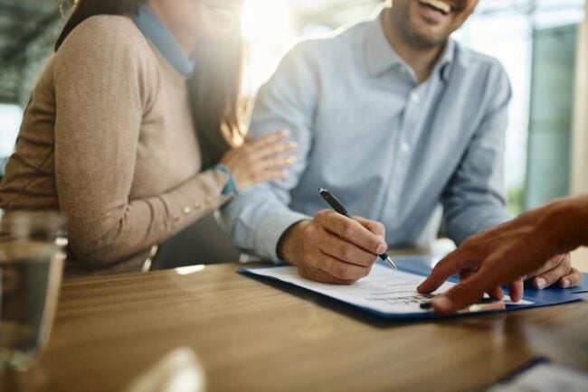 A man and a woman smile while signing a contract.