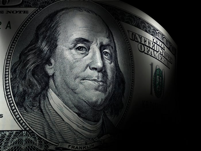 An up-close view of Ben Franklin's portrait on a one hundred dollar bill, which is set against a dark background.