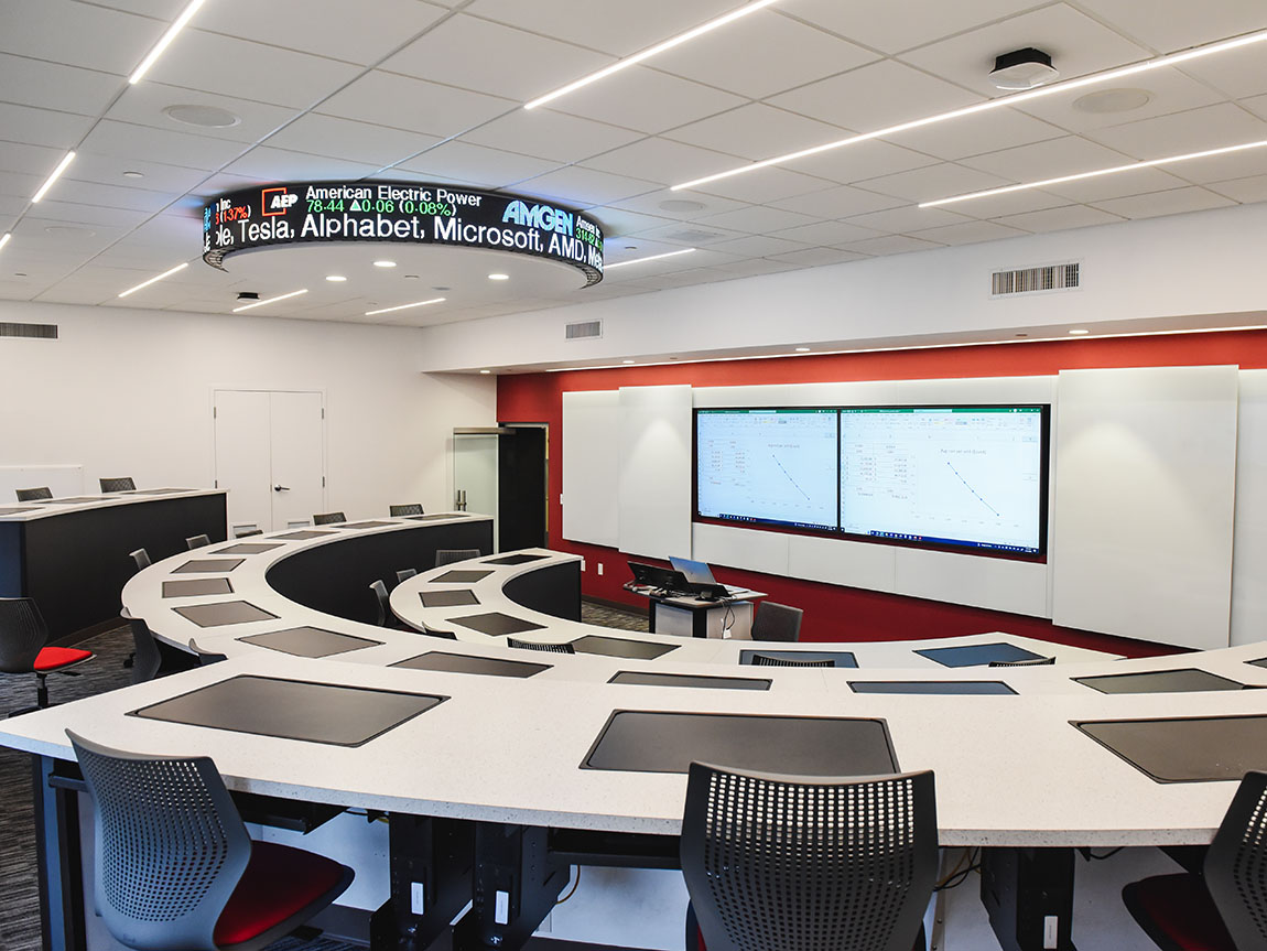 An empty classroom with stadium seating, big screens up front and a stock ticker on the ceiling