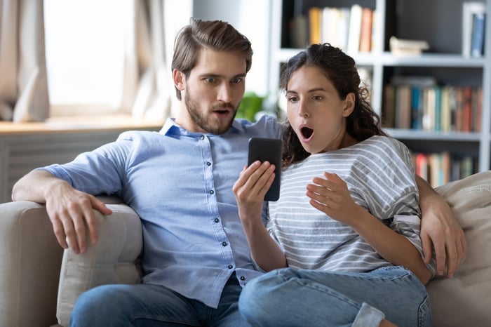 Two people looking at a phone with shocked expressions. 