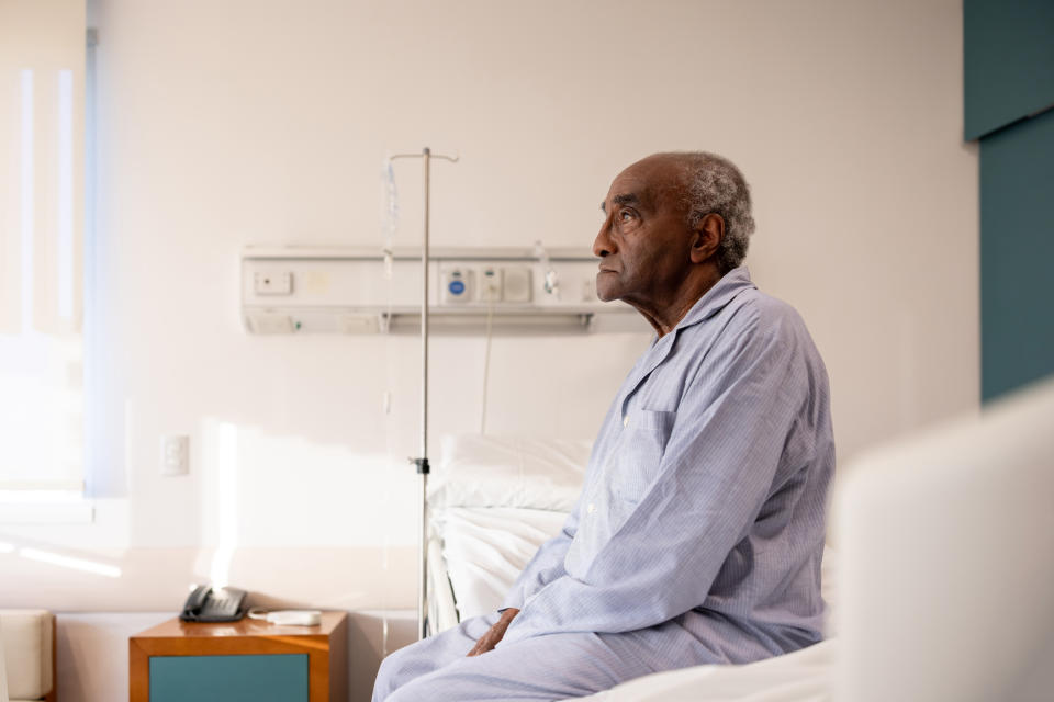 Sick senior man sitting on the edge of his bed at the hospital while hospitalized - healthcare and medicine concepts