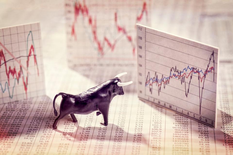 A bull figurine set atop a financial newspaper that's looking at a volatile popup stock chart.