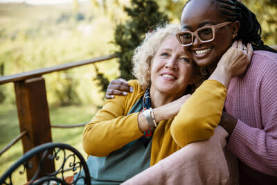 A senior white woman smiles as she leans into the shoulder of a Black woman wearing glasses. (CNW Group/Azrieli Foundation (The Canadian Centre for Caregiving Excellence))