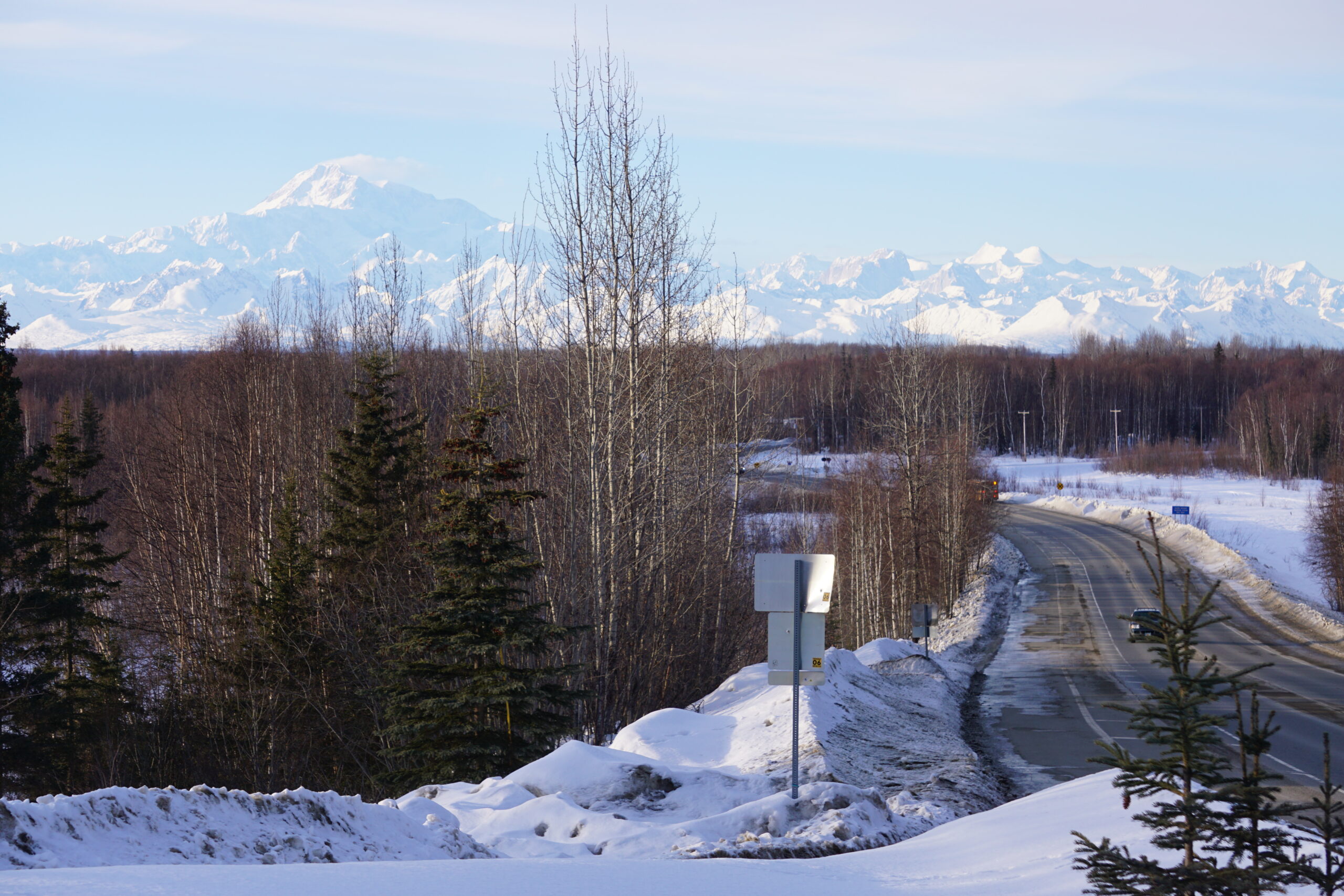 The Talkeetna spur road leading into community's downtown district is seen on March 9, 2024, with Denali and other Alaska Range mountains in the backdrop. (Photo by Yereth Rosen/Alaska Beacon)