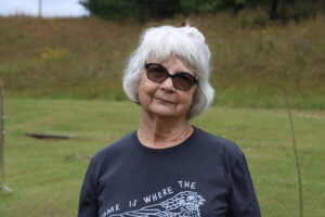Brenda Campbell wears black sunglasses and a shirt that reads, "Home Is Where The Whip-Poor-Will Sings."