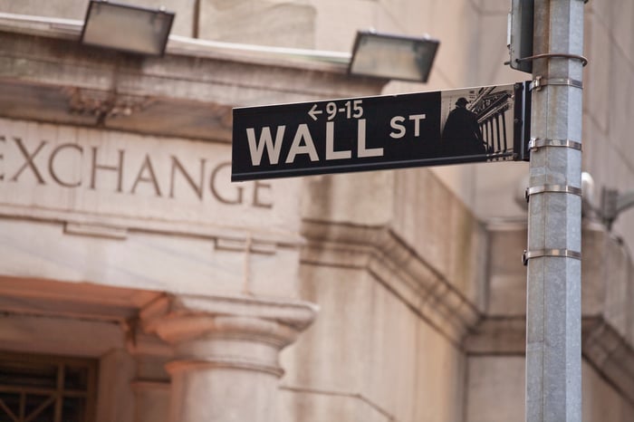 Wall St street sign in front of a stone building with Exchange etched over the door.