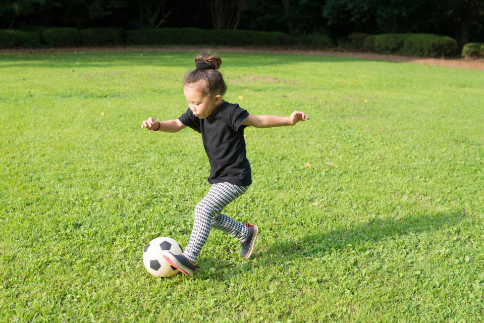 Child dribbling a soccer ball across a bright green field.
