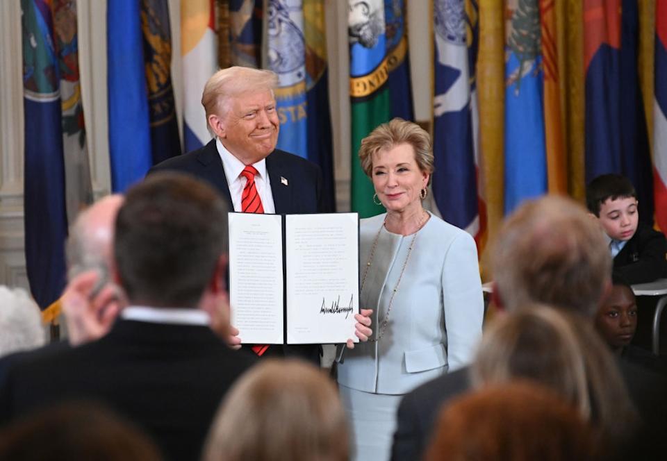 Two people stand together holding a signed document at an official event, surrounded by an audience