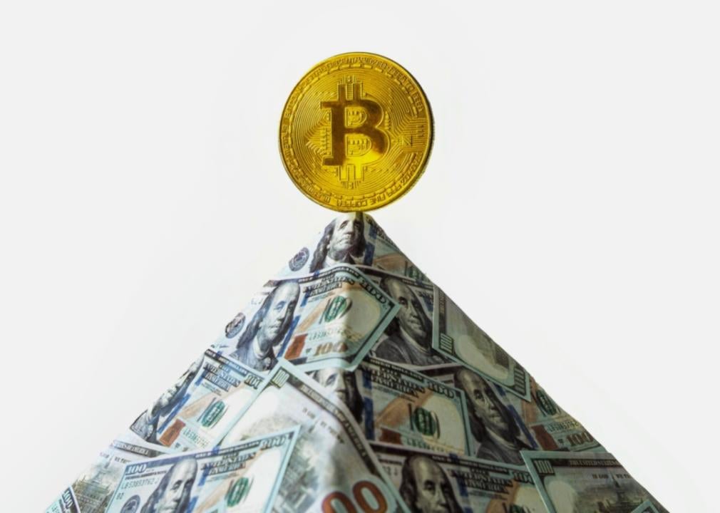 A pyramid made of U.S. dollar bills, topped with a golden bitcoin.