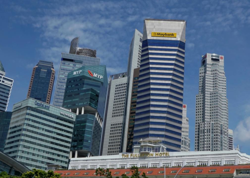 A cluster of modern skyscrapers in Singapore, including buildings with the names Maybank, MYP, CapitaLand, and WeWork, as well as The Fullerton Hotel.