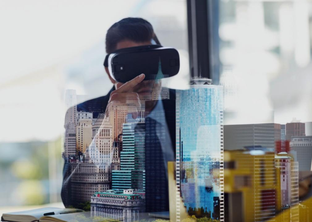 A man wearing virtual reality goggles, and in the foreground, a cityscape with modern skyscrapers is superimposed. 