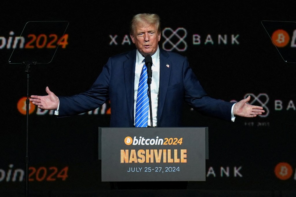 President Donald Trump gesturing at the Bitcoin 2024 event in Nashville, Tennessee while standing at a podium.