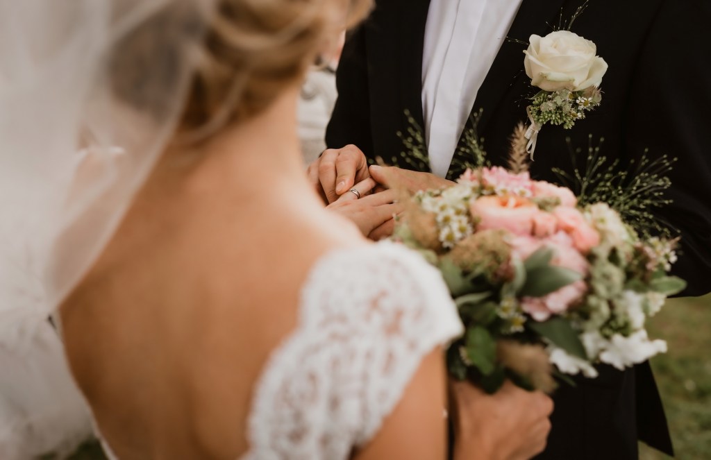 Groom placing wedding ring on bride's finger, focus on hands, foreground and background blurry