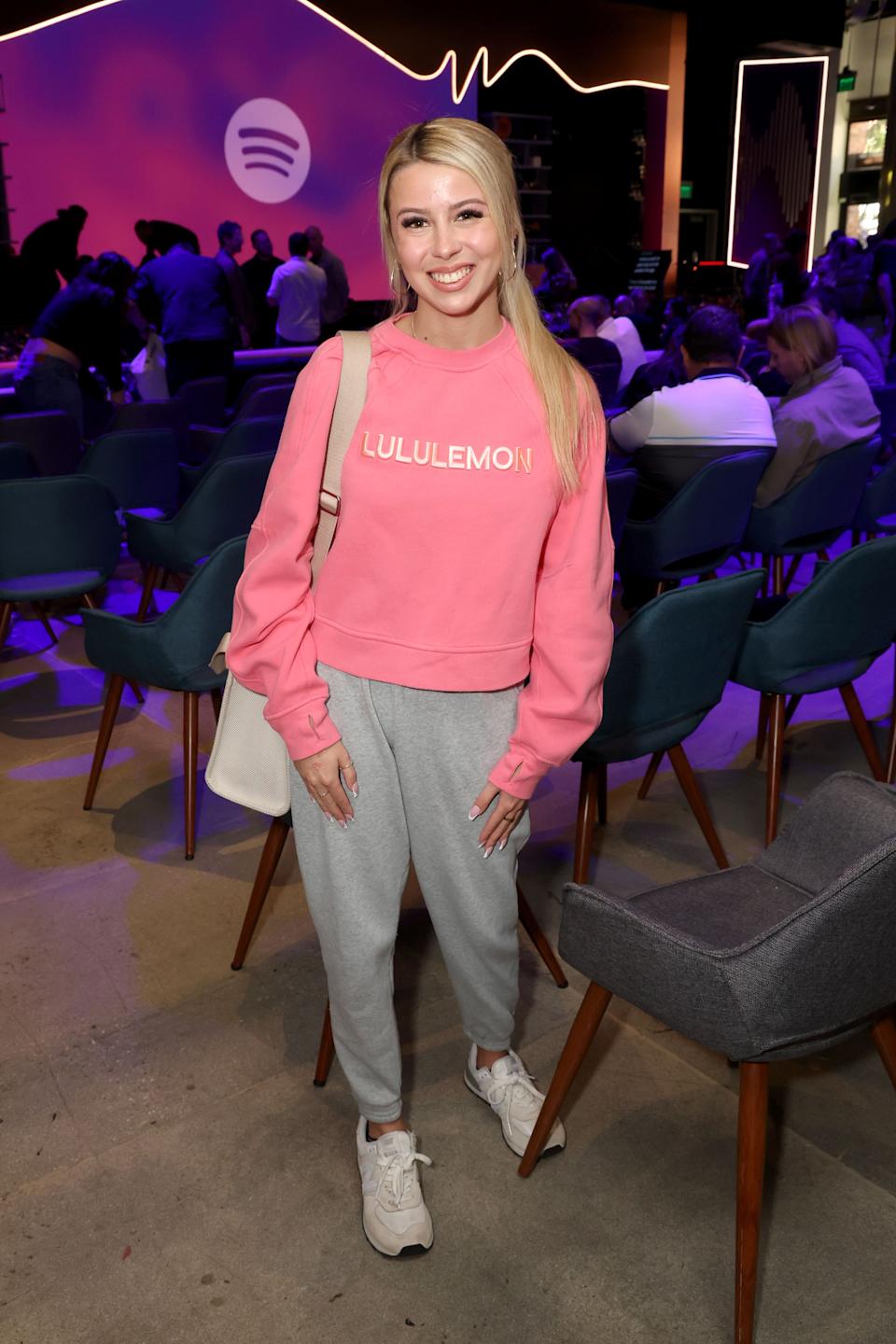 Haliey Welch wearing a casual Lululemon sweatshirt and pants at a Spotify event venue with seated attendees in the background
