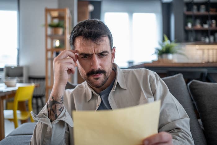 Person sitting on a couch, looking thoughtfully at a document, suggesting concentration on work or finances