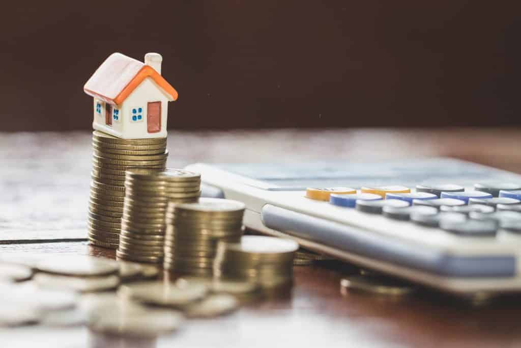 Cash, coins, a small house, and calculator sitting on a desk with mortgage documents.