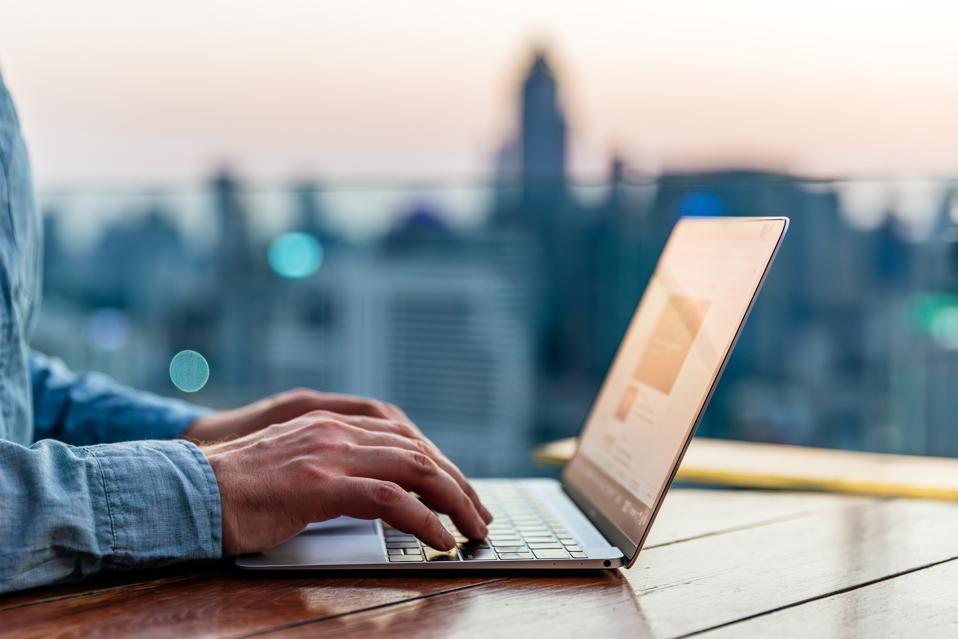Man typing on laptop keyboard with skyscrapers skyline in background