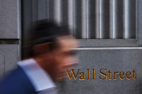 A man walks past a Wall Street marking outside the New York Stock Exchange (NYSE) building on Tuesday following Monday’s broad sell off in New York City