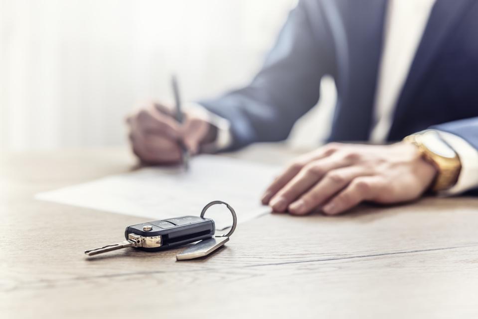 The agent signs a contract for the purchase or Leasing of a new car. New car keys in the foreground.