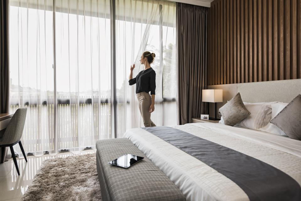 Young caucasian woman at home, looking out of  modern bedroom window