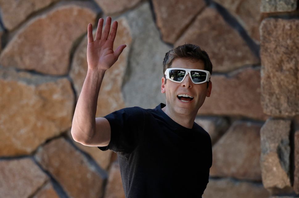 Man in black tshirt wearing white sunglasses waves to camera