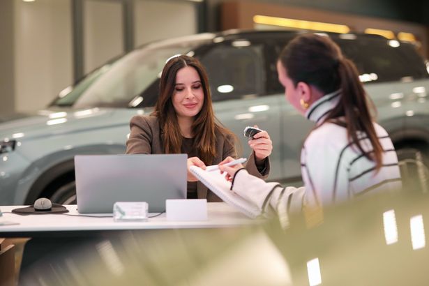 A woman is sitting in a car showroom talking to a sales person.