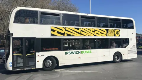 Alice Cunningham/BBC An Ipswich Buses double-decker bus exits Ipswich bus station. The bus is white with the company name on its side in green.