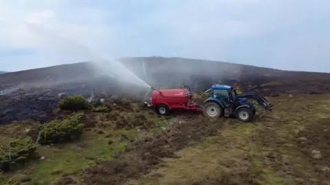 Alvie Estate A red slurry tank attached to the back of a tractor sits on a moorland spraying water across an area of burnt land